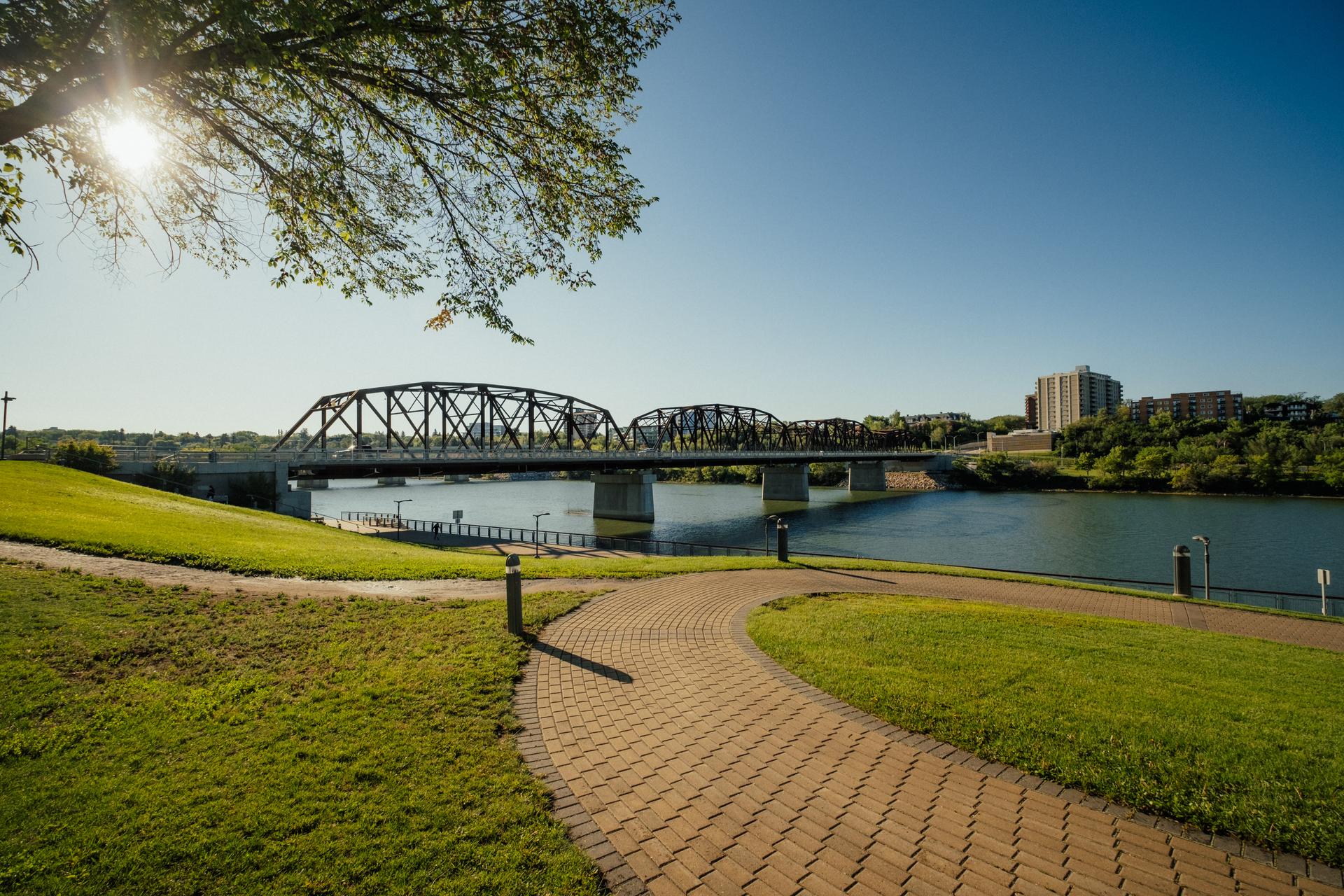 Walking path next to a river with a bridge spanning to the other side of the water