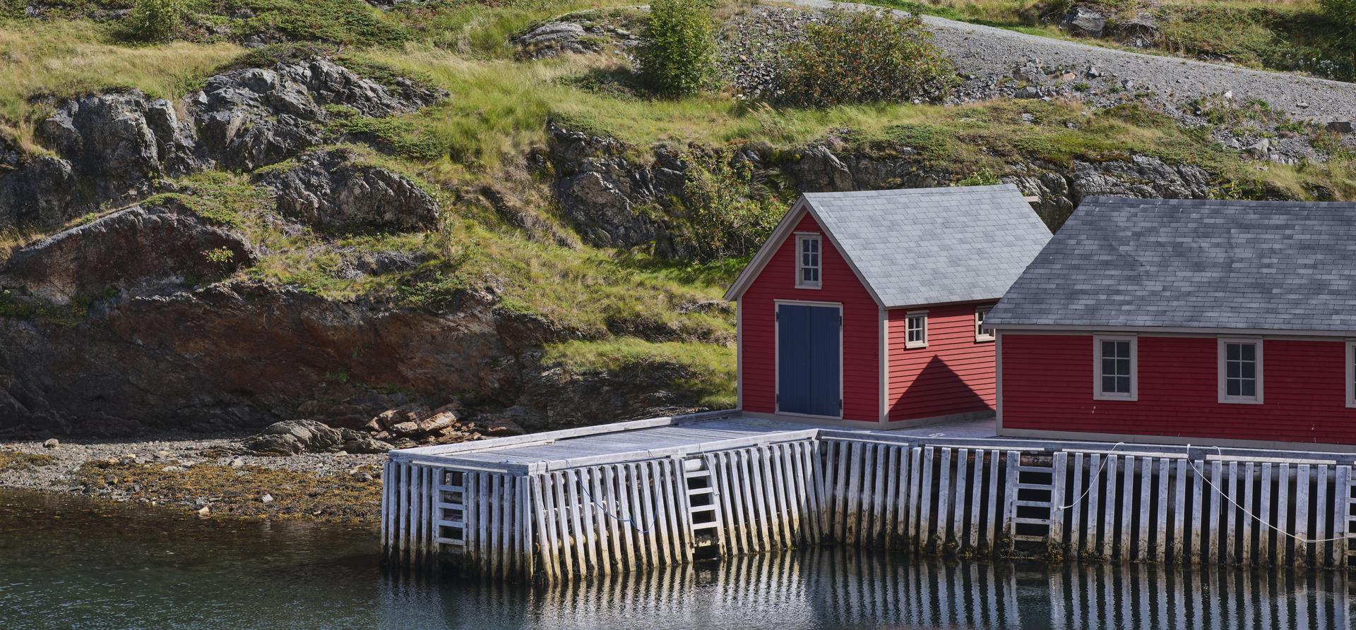 Red wooden boathouses sit beside a rocky shoreline