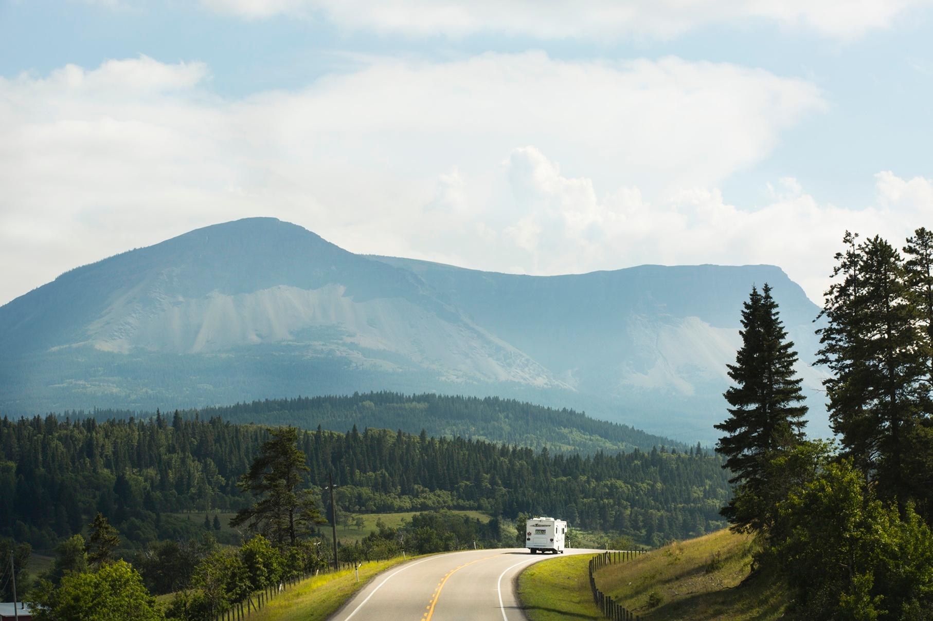 RV travelling along a winding road through a forested mountain landscape