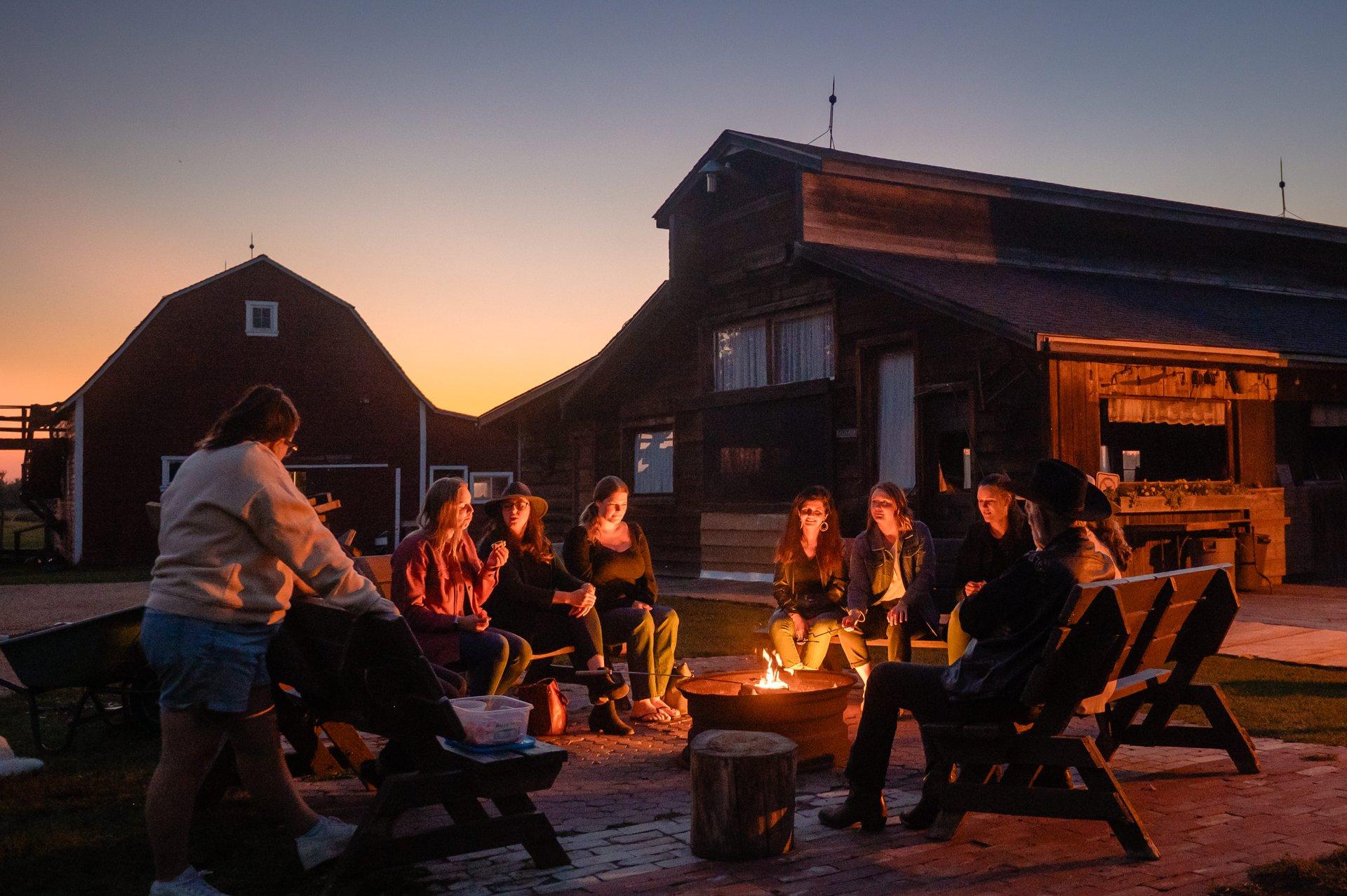Guests relaxing around a fire pit near a farmhouse