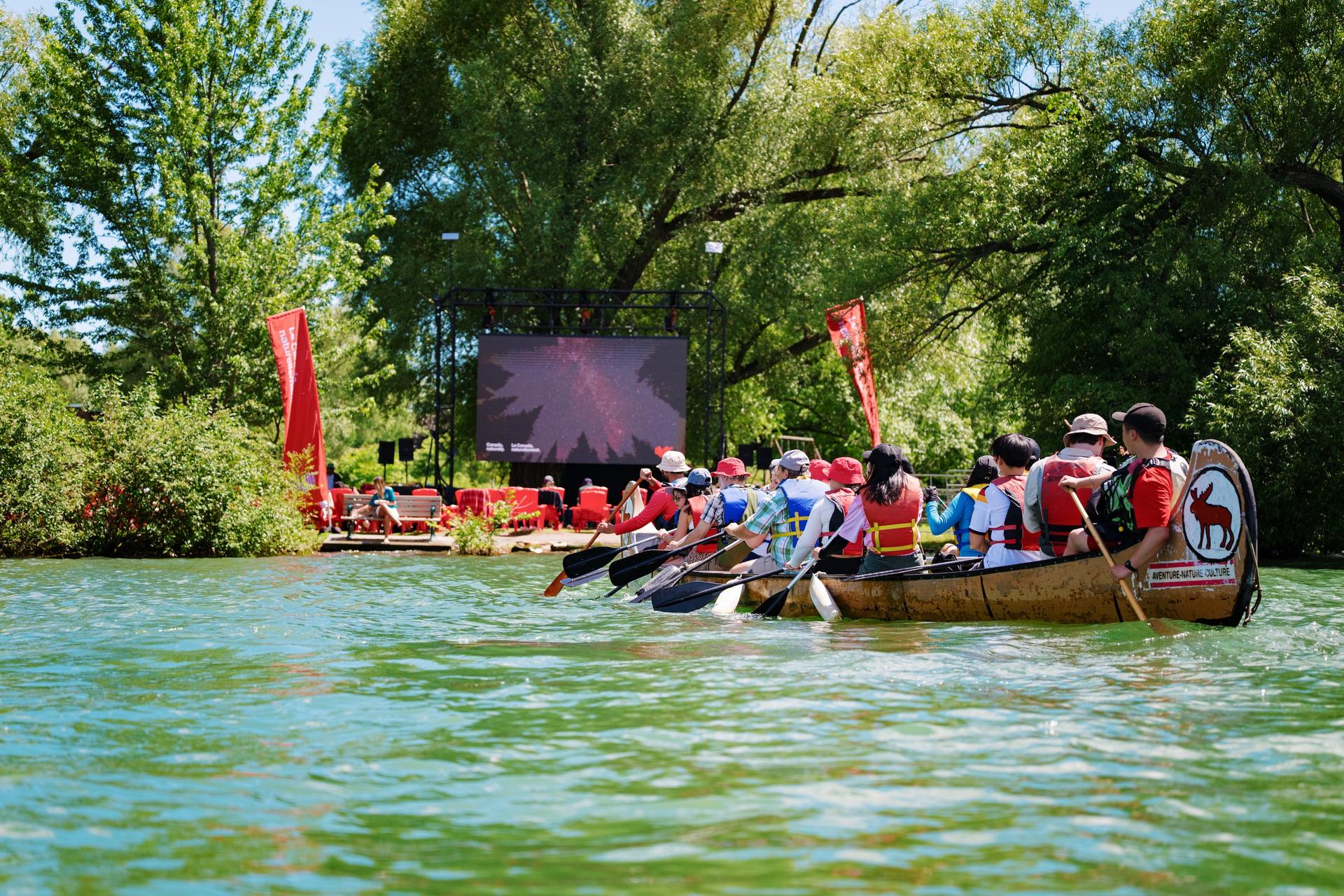 People paddling a canoe toward an outdoor screen