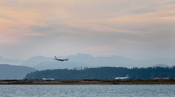 Airplane coming in for landing over the water at Vancouver International Airport with mountains in the background.