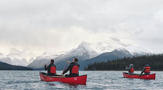 people paddling in red canoes on a lake with snow-capped rocky mountains in the background