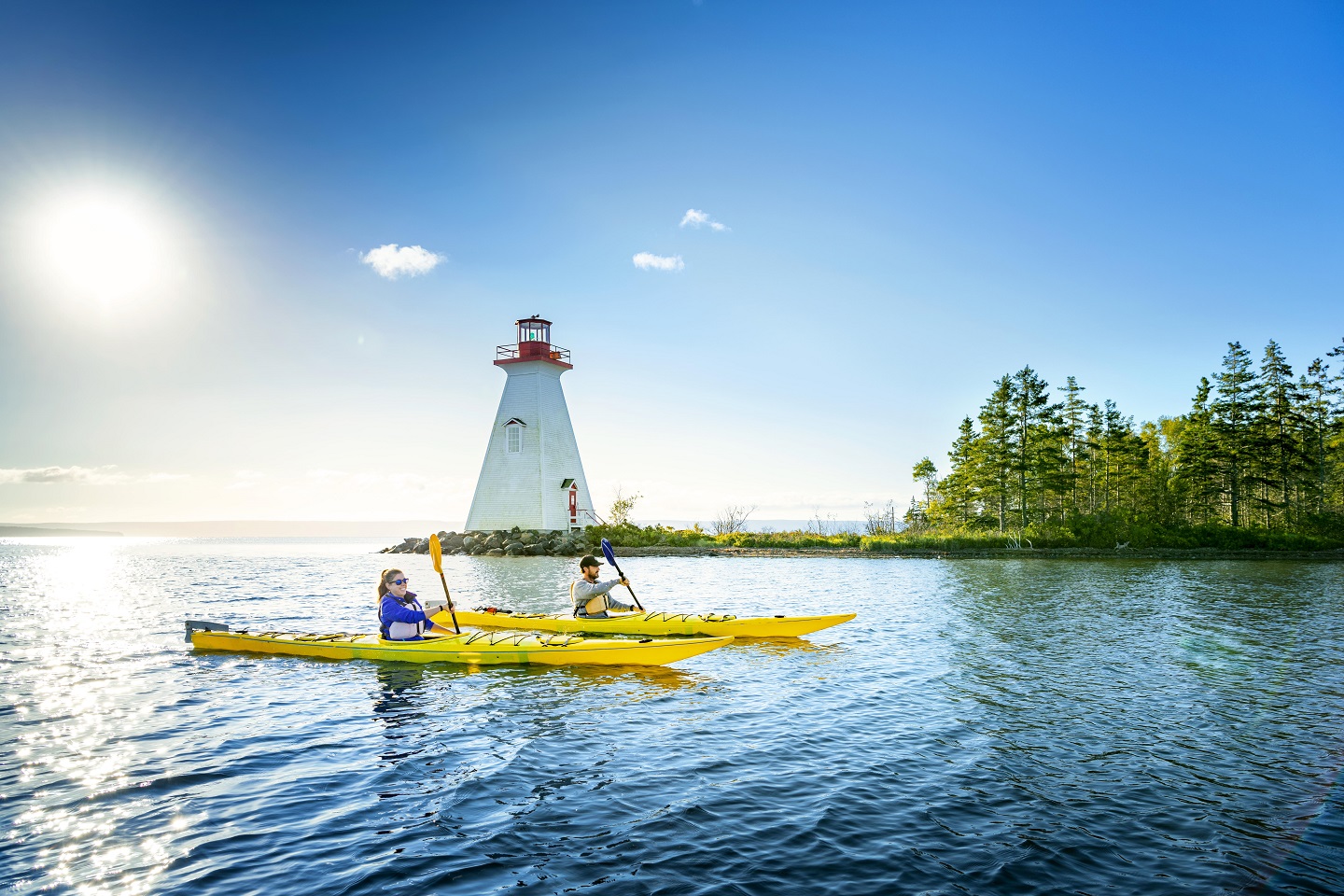 Deux personnes assises dans des kayaks jaunes à l’avant-plan et un phare à l’arrière-plan.