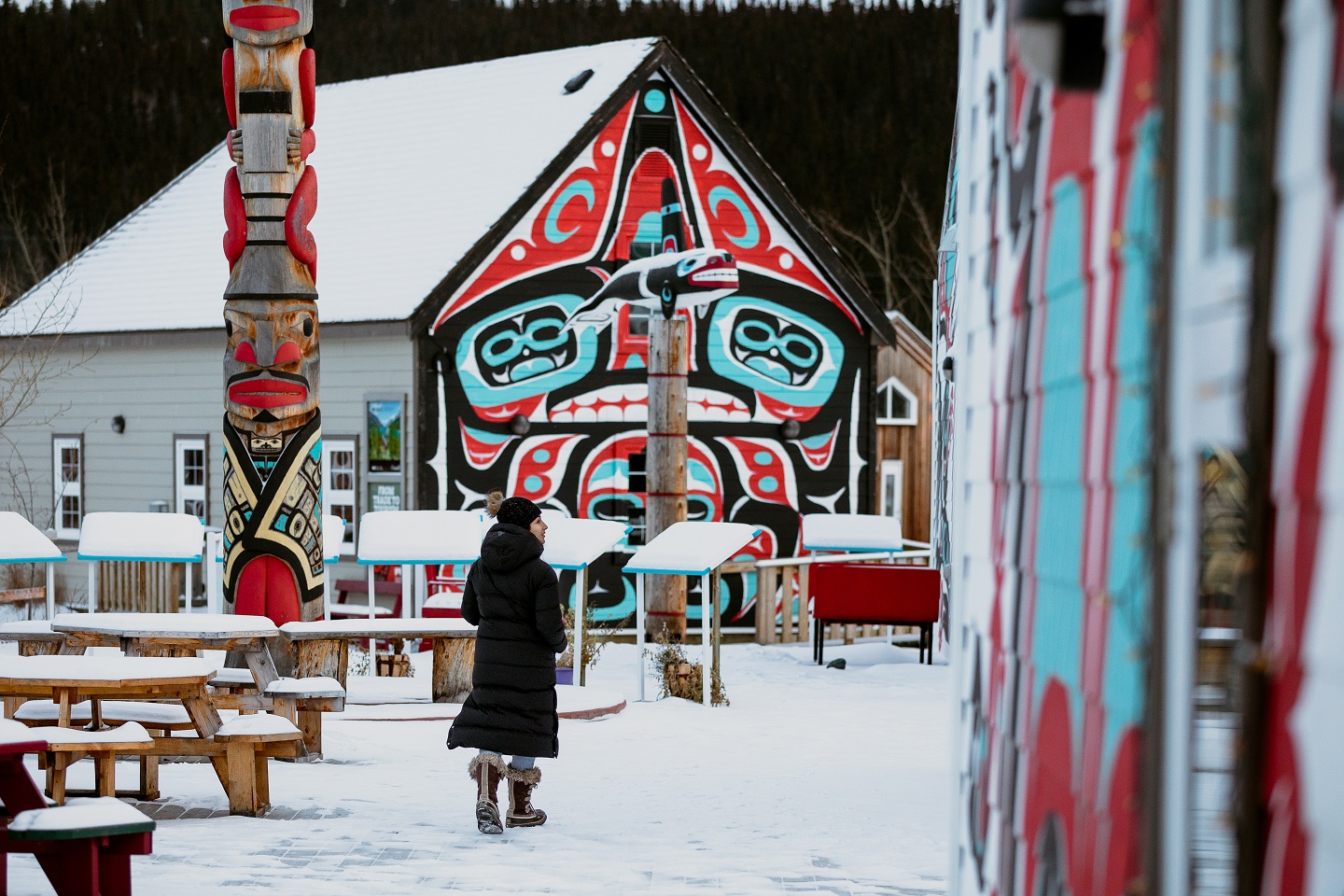 Une personne marche devant une murale et des œuvres autochtones dans un village enneigé.