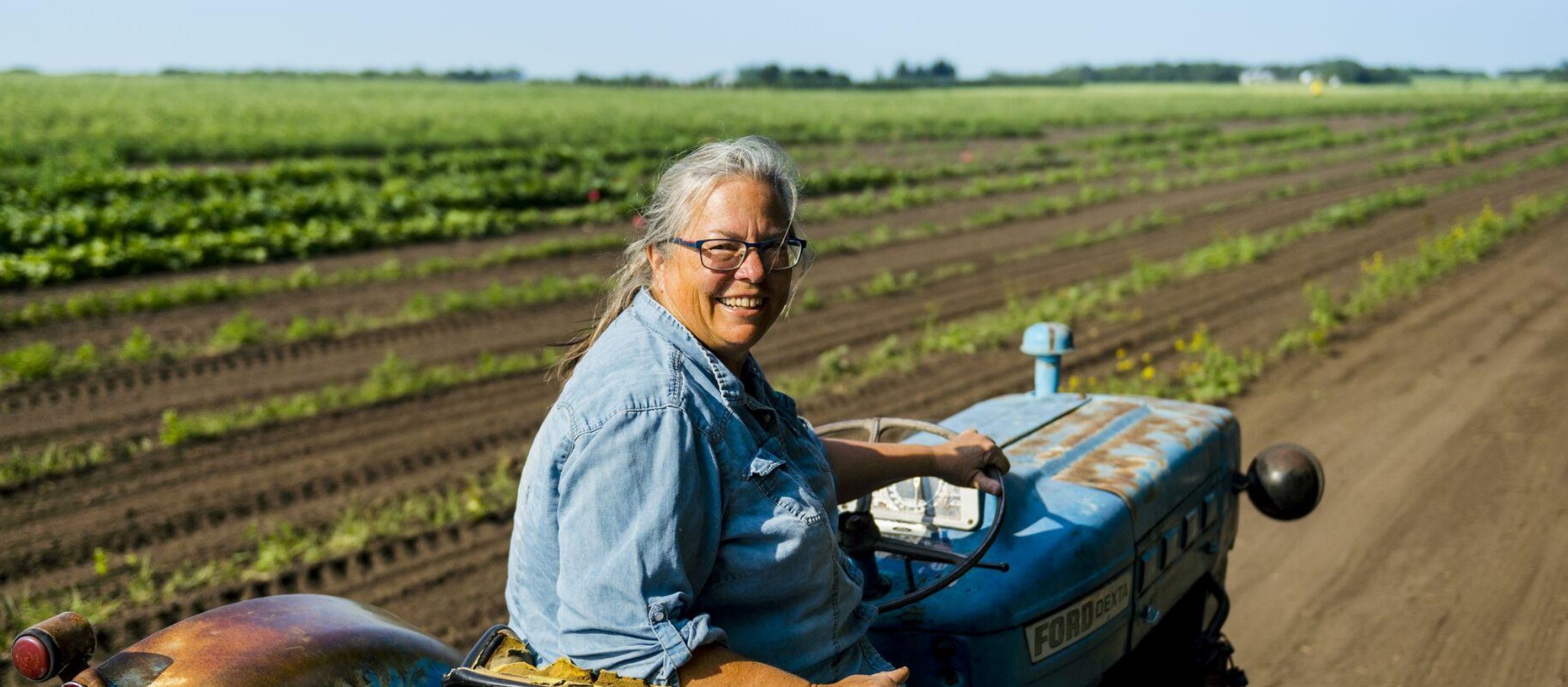 A person smiling while sitting on a tractor in a farm field.