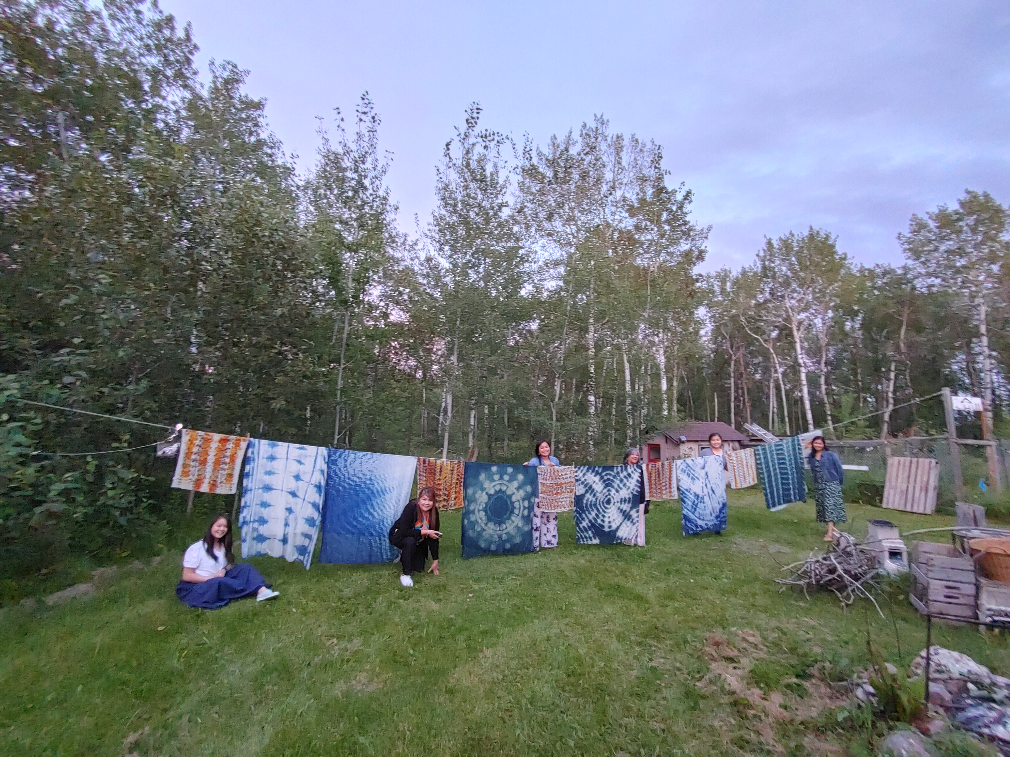 A group of people outside standing next to tapestries handing to dry