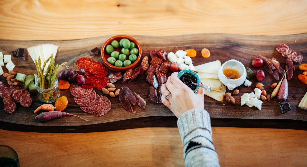 Wooden board covered in an assortment of fresh meats, vegetables, jams, and cheeses