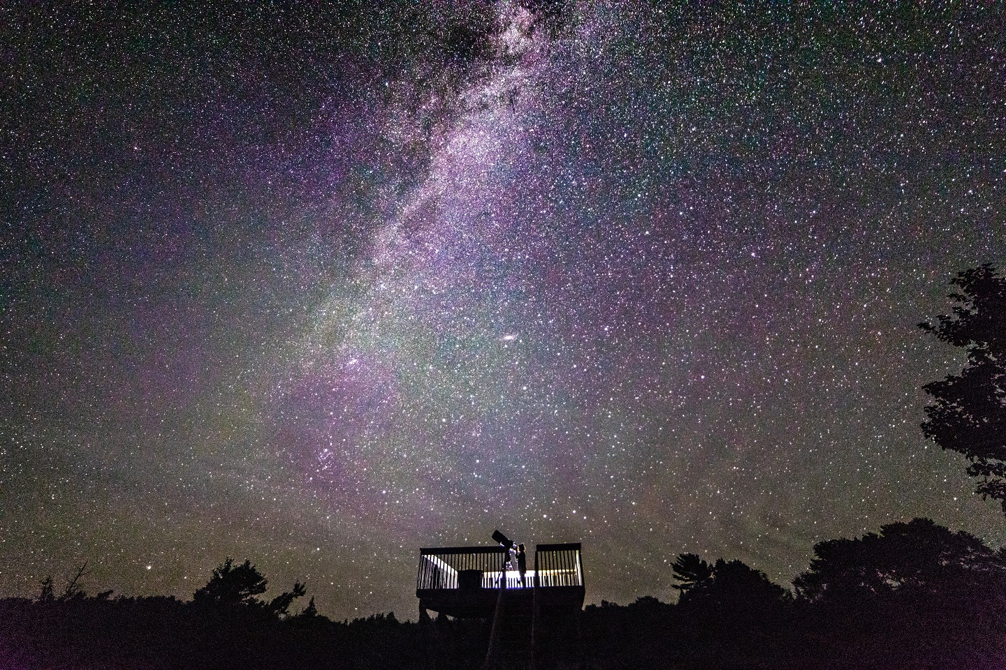Silhouette d’une personne qui regarde le ciel étoilé avec un télescope.