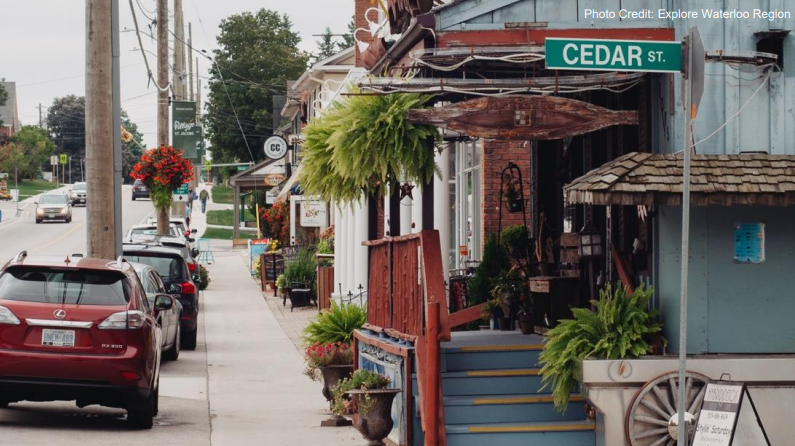 The image shows a street view of Cedar Street in St. Jacobs, featuring quaint shops with potted plants, parked cars, and people walking on the sidewalk.