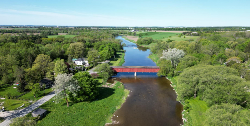 A picturesque aerial view of a serene river winding through lush green countryside, with a red bridge crossing it and scattered houses nearby.