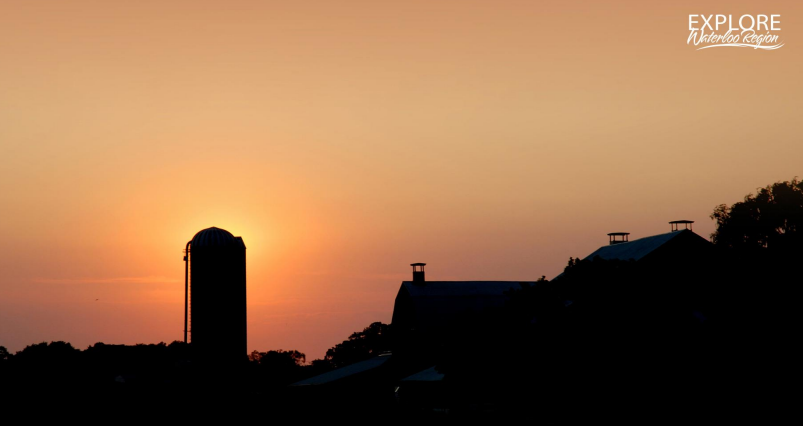 The image shows a serene sunset scene with the silhouette of a barn and silo against an orange sky, creating a peaceful rural atmosphere.