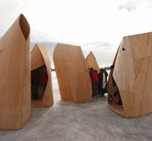 A photo shows people standing inside unique wooden warming huts on an icy surface at The Forks in Winnipeg.