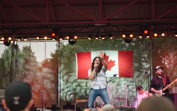 A photo shows a live musical performance on a stage at The Forks in Winnipeg, with a singer and band performing in front of a Canadian flag backdrop and an audience watching.