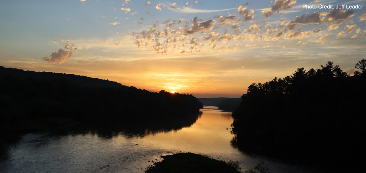 A photo shows a serene river at sunset, with the sky filled with clouds and the surrounding landscape silhouetted against the golden light, credited to Jeff Leader.