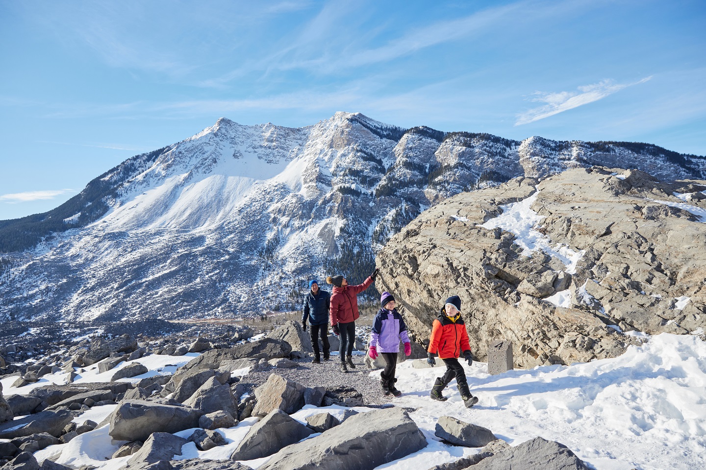 A family of four hikes on a snowy path with mountains in the background. 