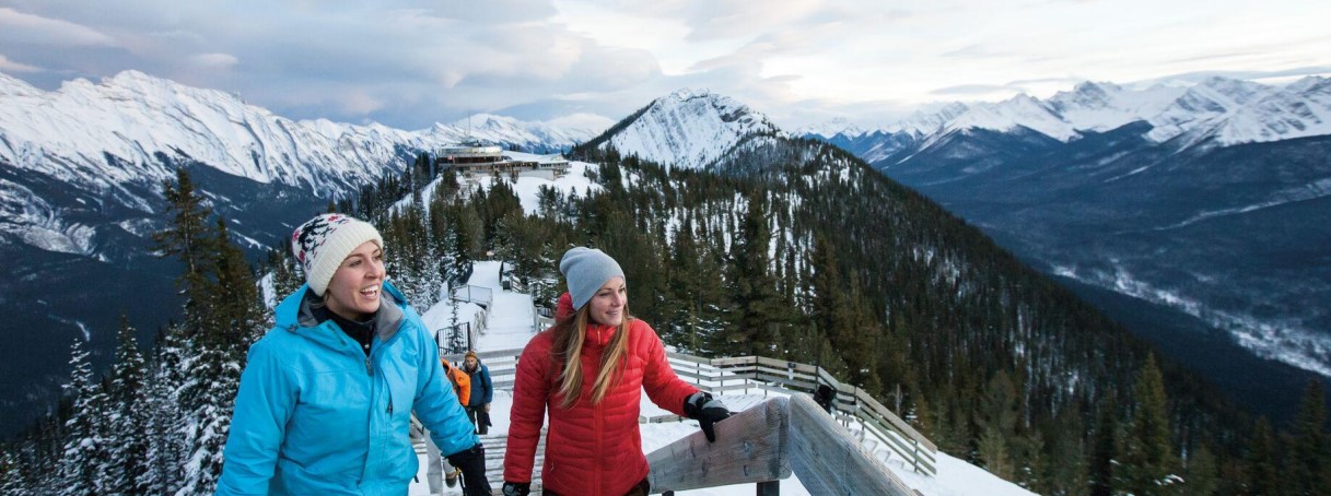 Two people walking along snow-filled mountains 