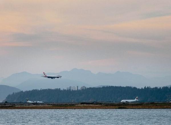 Airplane coming in for landing over the water at Vancouver International Airport with mountains in the background.